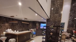 Una hall moderna di un hotel con una reception in marmo, area salotto e un grande schermo televisivo.
