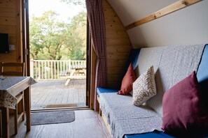 L’intérieur d’un chalet accueillant, avec une terrasse en bois, un canapé agrémenté de coussins à motifs et une table à manger.