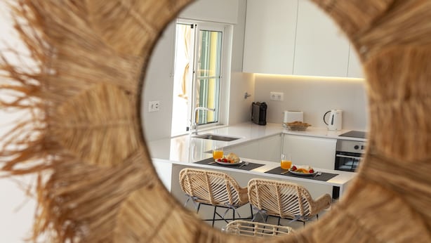 A modern kitchen with white cabinetry, a central island with seating, and a view through a circular mirror. - Townhouse w/ Rooftop & Sea View in Benagil (Benagil)