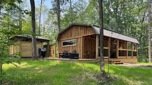 A rustic cabin with a deck, outdoor seating, and a grill area.