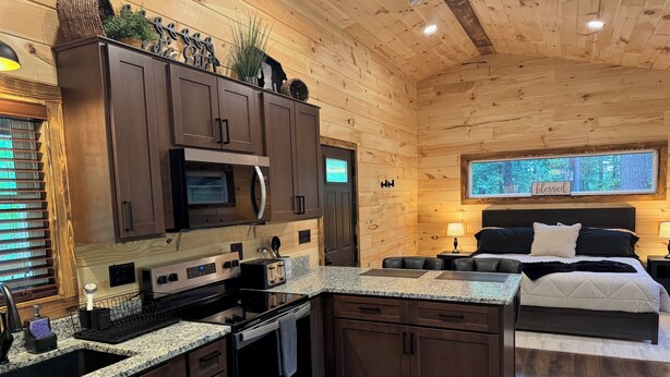 A compact, modern kitchen with dark wood cabinets, a built-in microwave, and a granite countertop.
