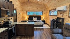 A cozy log cabin interior with a kitchenette, a bed with a view, and a seating area.