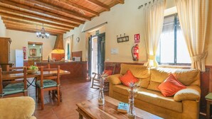 A cozy living room with a sofa, chairs, a coffee table, and a dining area with a table and chairs. There is a kitchen visible in the background. - Casa Rural La Dehesilla Cazalla de la Sierra by Ruralidays (Seville)