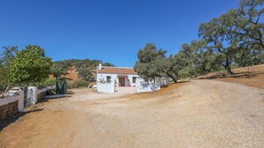 A white house with a tiled roof, surrounded by gravel and trees, with a clear sky above. - Casa Rural La Dehesilla Cazalla de la Sierra by Ruralidays (Seville)