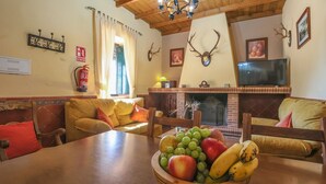 A cozy living room with a fireplace, a dining table with fruit, and a sofa with cushions. - Casa Rural La Dehesilla Cazalla de la Sierra by Ruralidays (Seville)