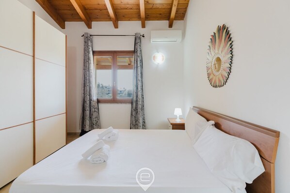 A hotel room with a bed, a window with curtains, a wall-mounted lamp, and a decorative wall piece.