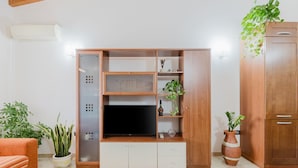 Un soggiorno con una TV su un mobile in legno, un divano e piante in vaso.