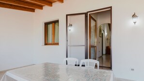 Una stanza con un tavolo grande, due sedie bianche, una finestra con tende e una porta che dà su un'altra stanza.