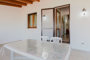 Une pièce comprenant une grande table, deux chaises blanches, une fenêtre avec des rideaux et une porte donnant sur une autre pièce.