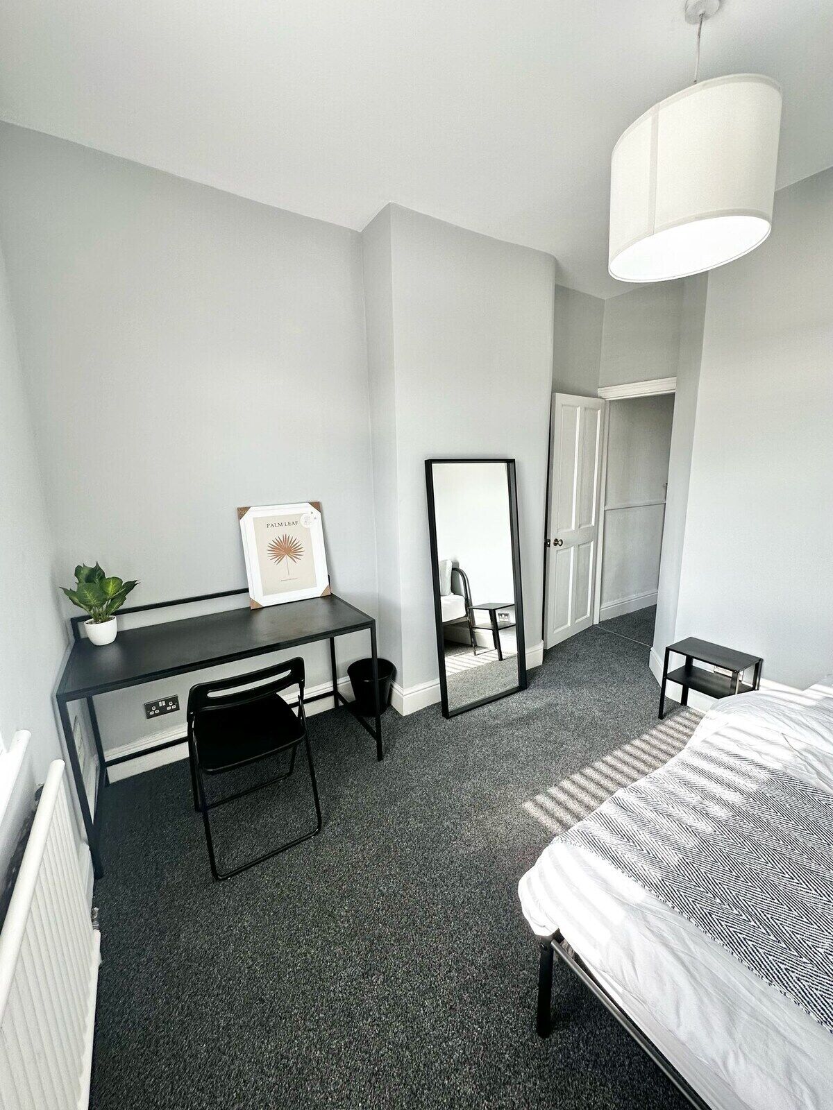 Una habitación de hotel moderna con una cama, un escritorio, una silla, un espejo y una planta en maceta.