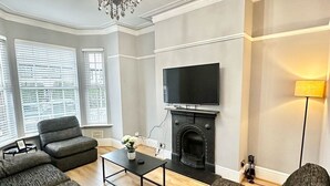 A living room with a fireplace, a television, and two sofas. - Luxury 5 bed salford home (free parking) (Salford)