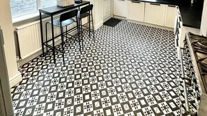 A kitchen with white cabinets, a black countertop, and a patterned floor. - Luxury 5 bed salford home (free parking) (Salford)