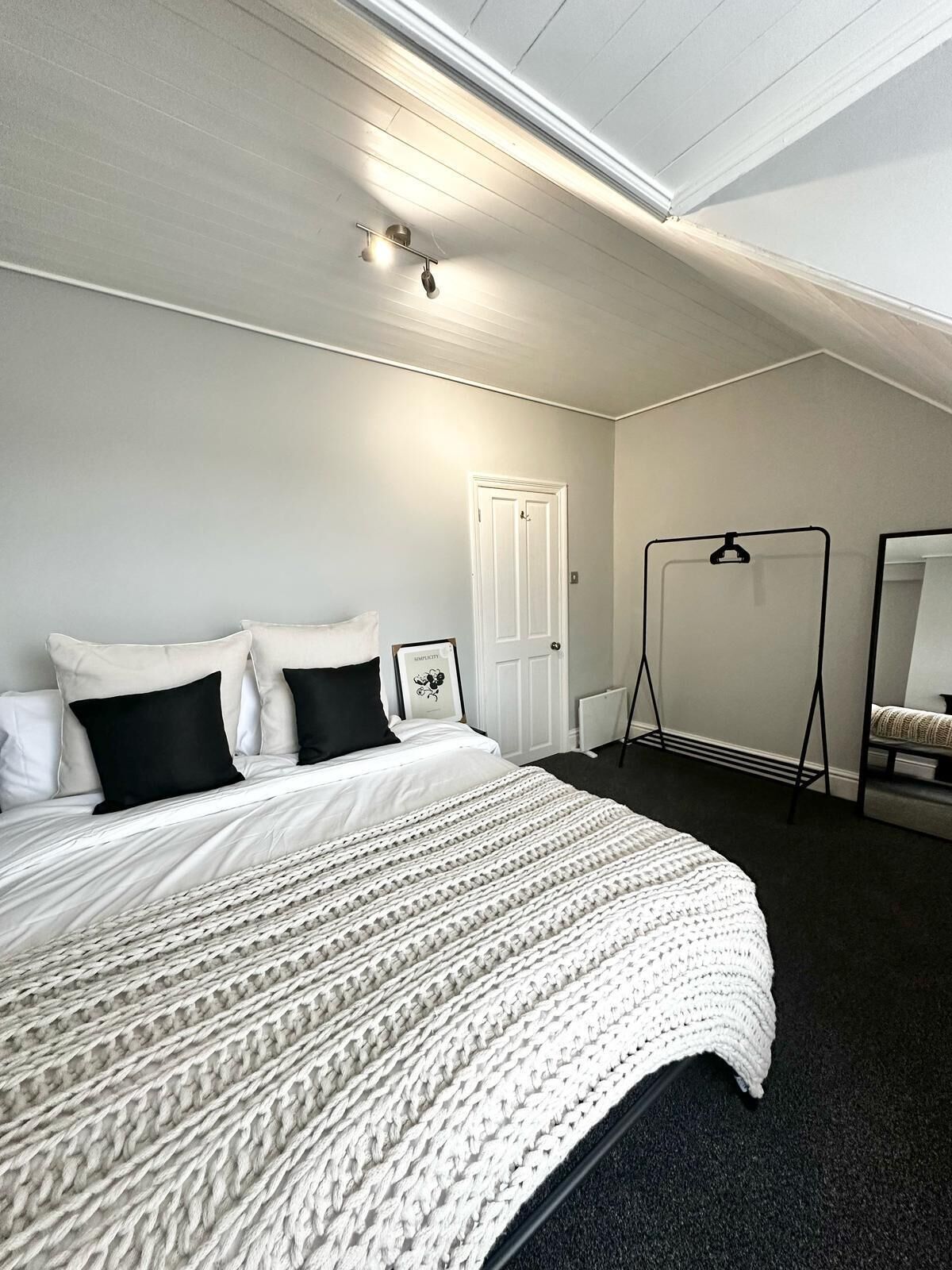 A bedroom with a bed, a white door, a black hanger, and a mirror.