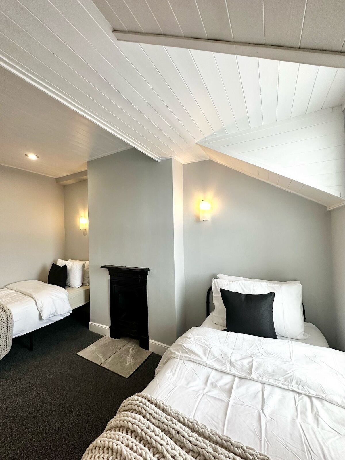 A hotel room with two beds, a dark-colored nightstand, and a light-colored woven throw blanket.