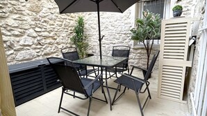 A stone-walled outdoor patio with a glass table and chairs, a large umbrella, and potted plants. - Le Cosy Nîmois, charm & terrace in the heart of Nîmes, 4 minutes from the arena (Nîmes)