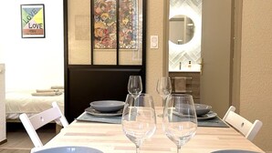 A dining area with a table set for two, featuring blue plates and wine glasses. A framed poster with cartoon characters is on the wall, and a sliding door leads to another room. - Le Cosy Nîmois, charm & terrace in the heart of Nîmes, 4 minutes from the arena (Nîmes)