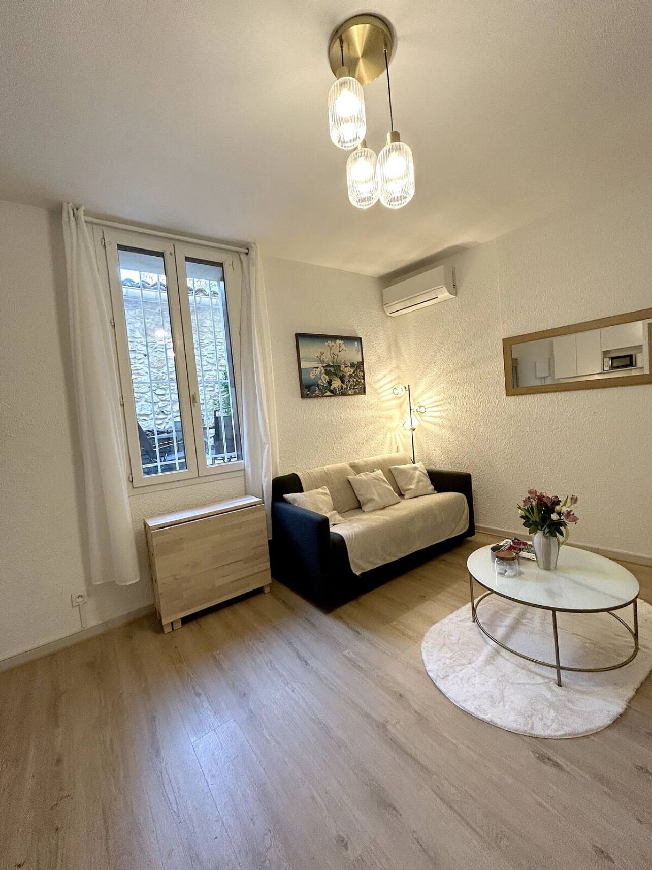 A living room with a sofa, a round coffee table, a radiator, a window with curtains, and a painting on the wall.