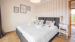 Un letto rifatto con lenzuola bianche, una testiera grigia e un comodino con una lampada. Al muro, tre quadri incorniciati.