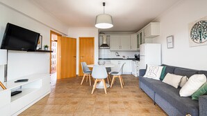 Un soggiorno moderno con un divano grigio, un tavolo da pranzo con sedie, una TV su un mobile e una zona cucina sullo sfondo.