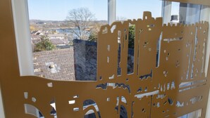 A window with a cut-out design of a castle, overlooking a town with buildings and a river.