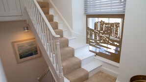 A staircase with beige carpeted steps and white railings, a framed picture on the wall, and a window with blinds.