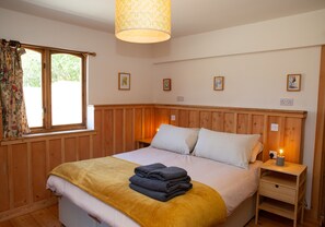 A bedroom with a wooden headboard, a bed with a yellow blanket, a bedside table with a lamp, and a window with curtains.