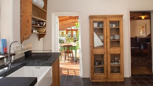 Une cuisine avec des meubles de rangement en bois, un évier et un coin repas visible à travers une porte ouverte.