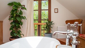 Une salle de bain avec une baignoire, une plante en pot, une fenêtre avec des rideaux et une chaise en bois.