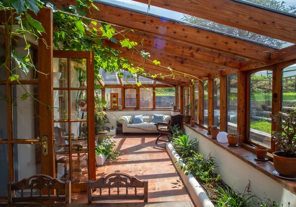 A sunlit room with a wooden ceiling, a sofa, a bench, and potted plants.