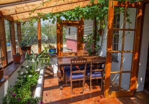 A covered patio with a wooden table and chairs, surrounded by potted plants and a small garden.