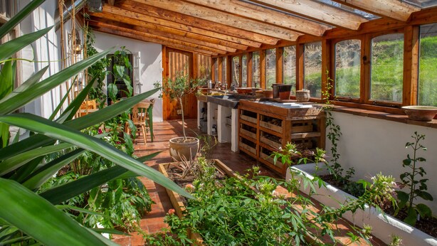 Un espace cuisine extérieur abrité, doté de poutres en bois, de plantes en pot et d’une table en bois rustique.