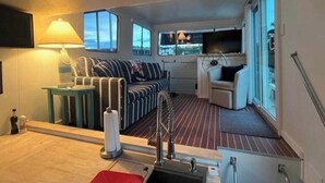 En kompakt opholdsstue med sofa, lille bord med lampe, fjernsyn og et vindue med udsigt.