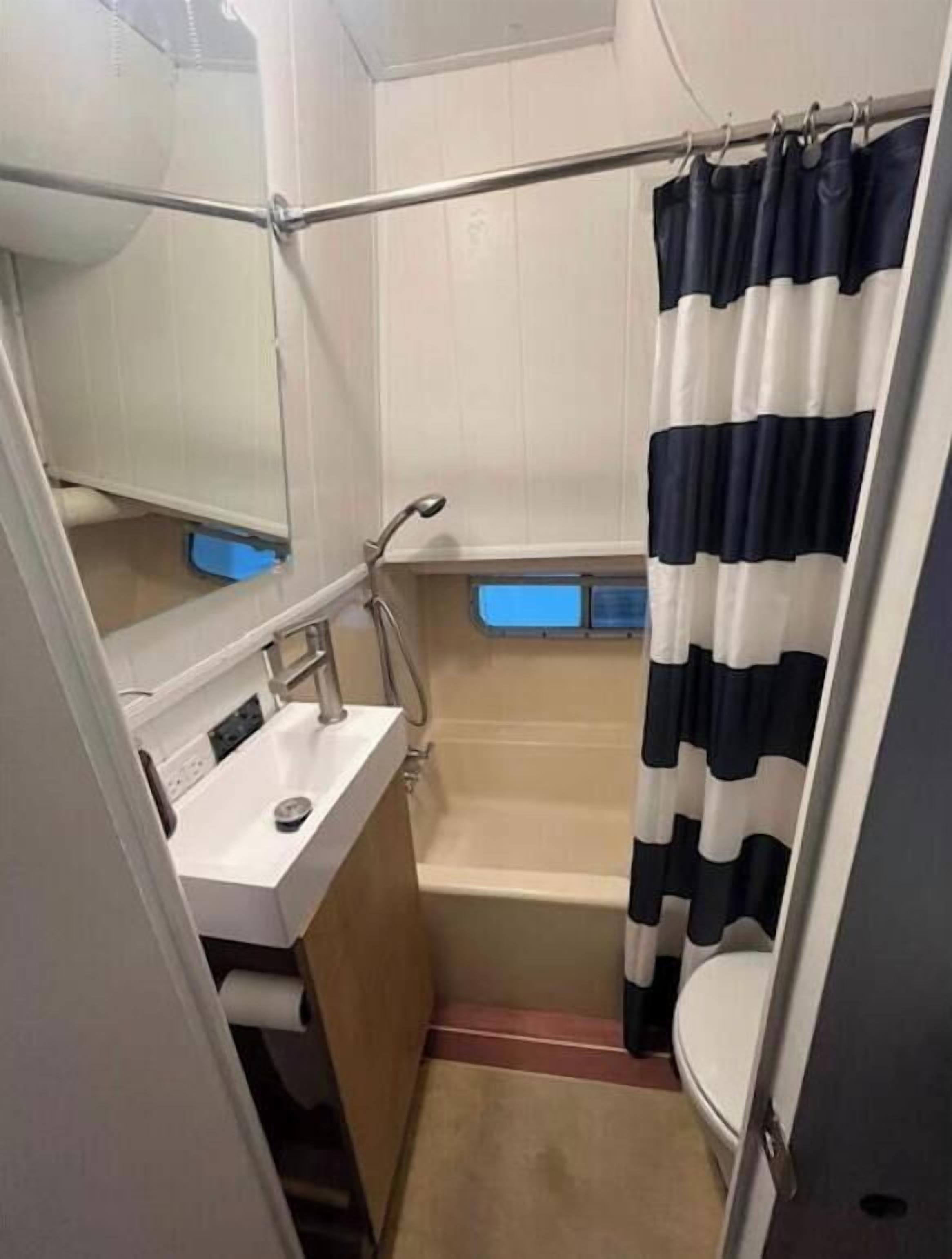 Une petite salle de bain avec un lavabo blanc, un miroir, une douche et un rideau de douche à rayures noires et blanches.