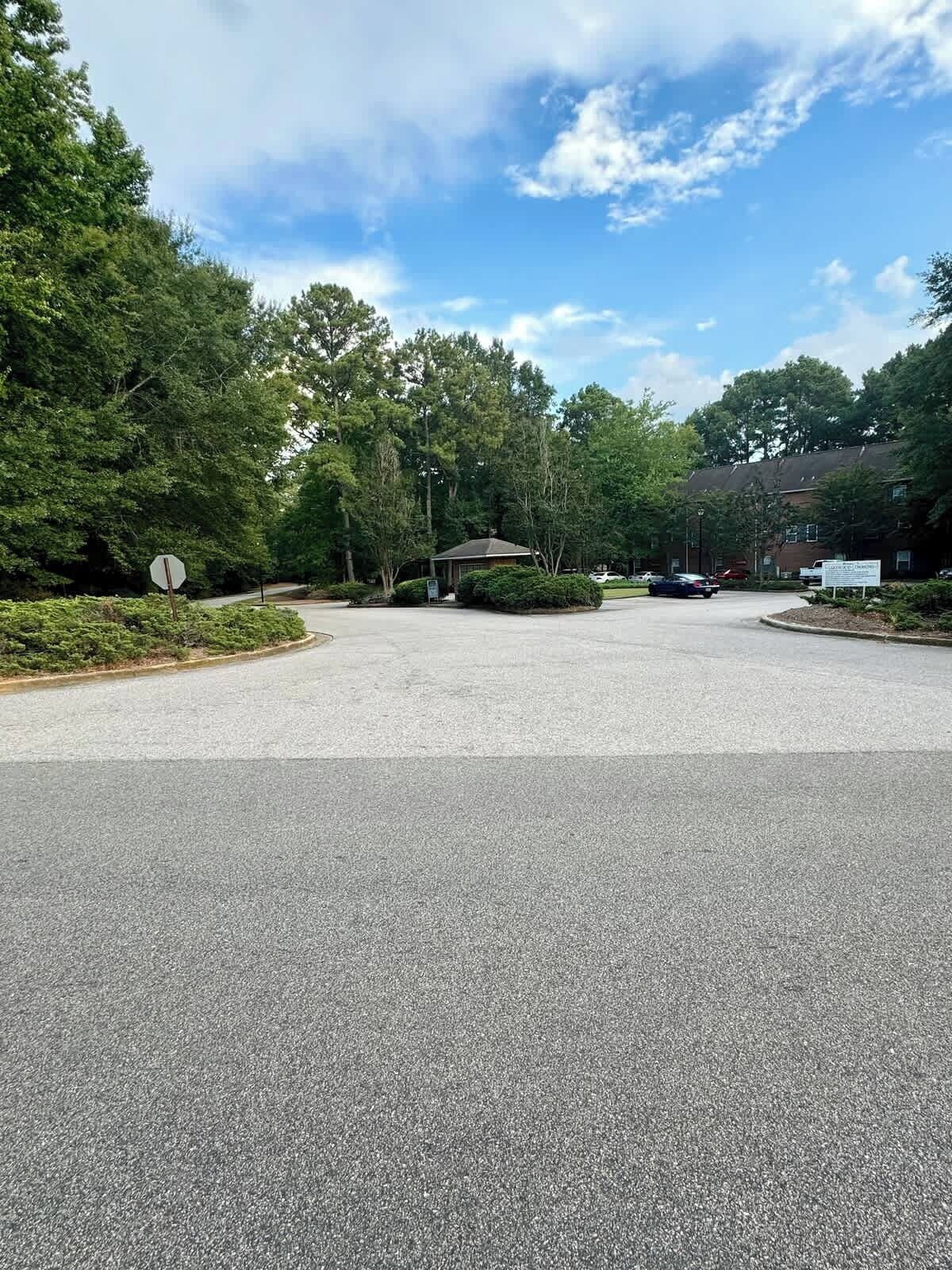 Un parking avec un panneau de signalisation « stop », entouré d’arbres et avec un bâtiment en arrière-plan.