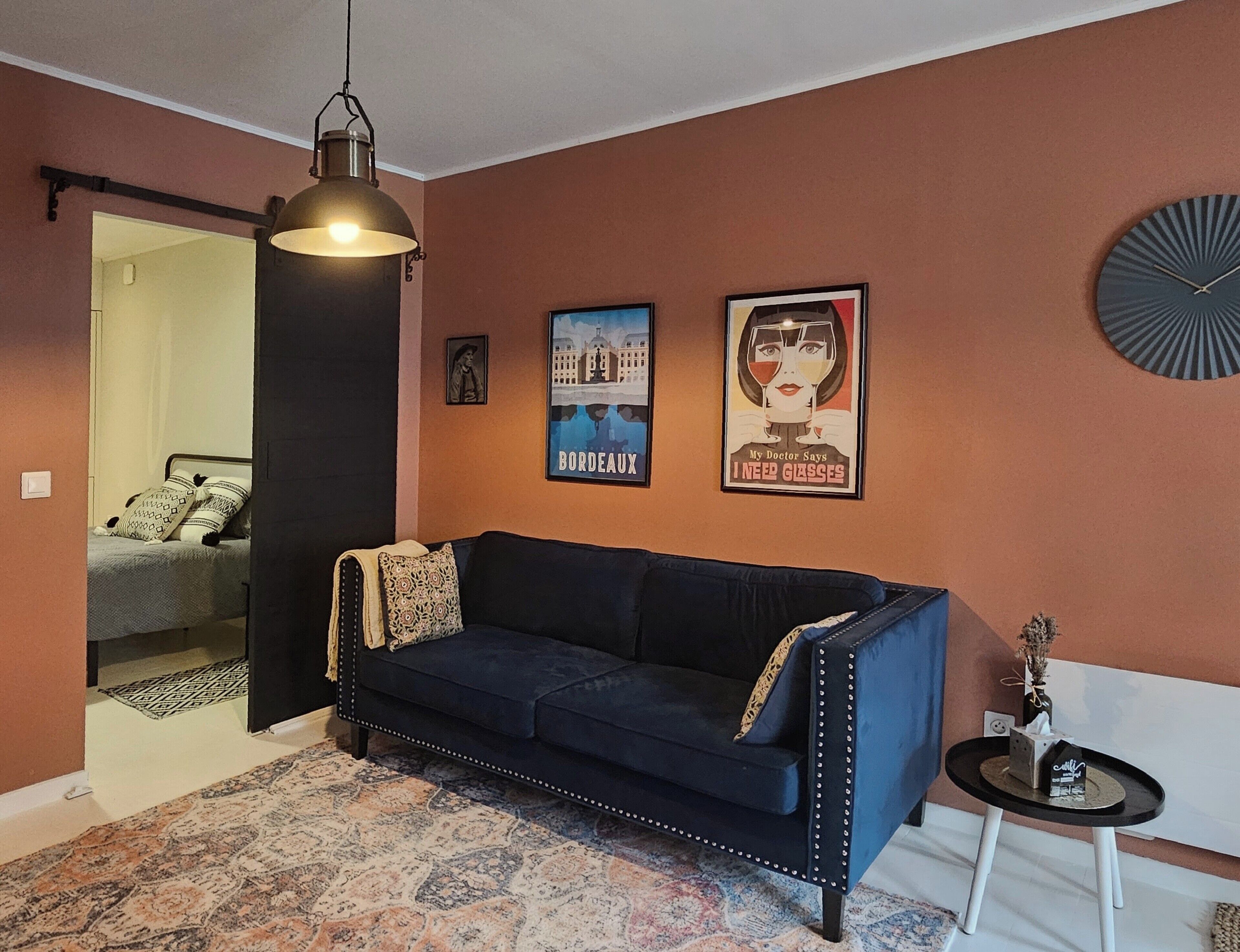 A room with a dark blue sofa, a patterned rug, a hanging light fixture, and two framed posters on the wall.