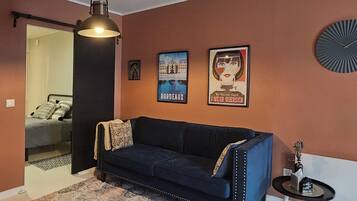 A room with a dark blue sofa, a patterned rug, a hanging light fixture, and two framed posters on the wall.