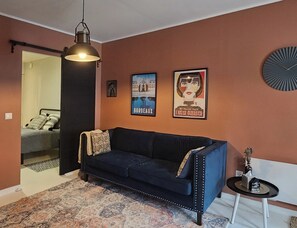 Una stanza con un divano blu scuro, un tappeto decorato, un lampadario e due poster incorniciati alle pareti.