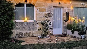 A stone building with a tiled roof, a white door, and a window with a lamp on the sill. - Maison Finchette • 5 min f Saint-Émilion • Private Terrace • Parking • For 2 (Sainte-Terre)