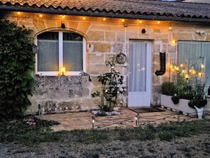 A stone building with a tiled roof, a white door, and a window with a lamp on the sill.