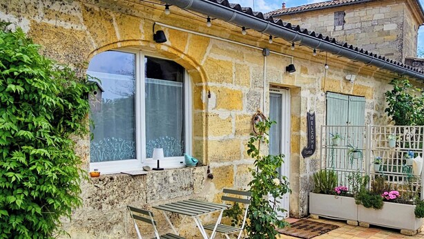 A stone building with a tiled patio, a small table and chairs, and a garden area with plants and flowers. - Maison Finchette • 5 min f Saint-Émilion • Private Terrace • Parking • For 2 (Sainte-Terre)
