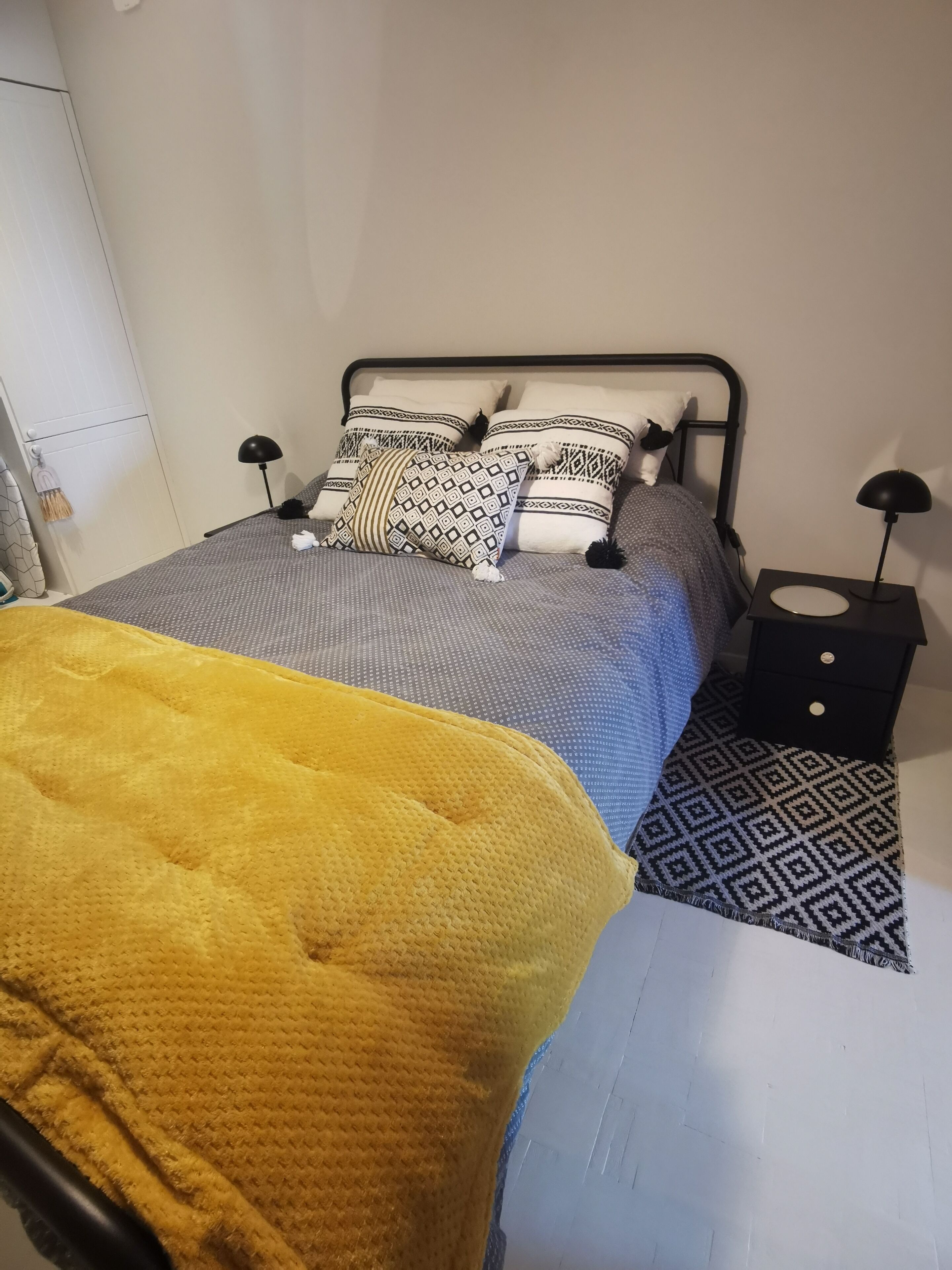 Una cama con ropa de cama estampada, un plaid amarillo y dos mesitas de noche con lámparas.