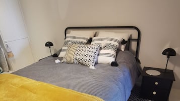 Una cama con ropa de cama estampada, un plaid amarillo y dos mesitas de noche con lámparas.