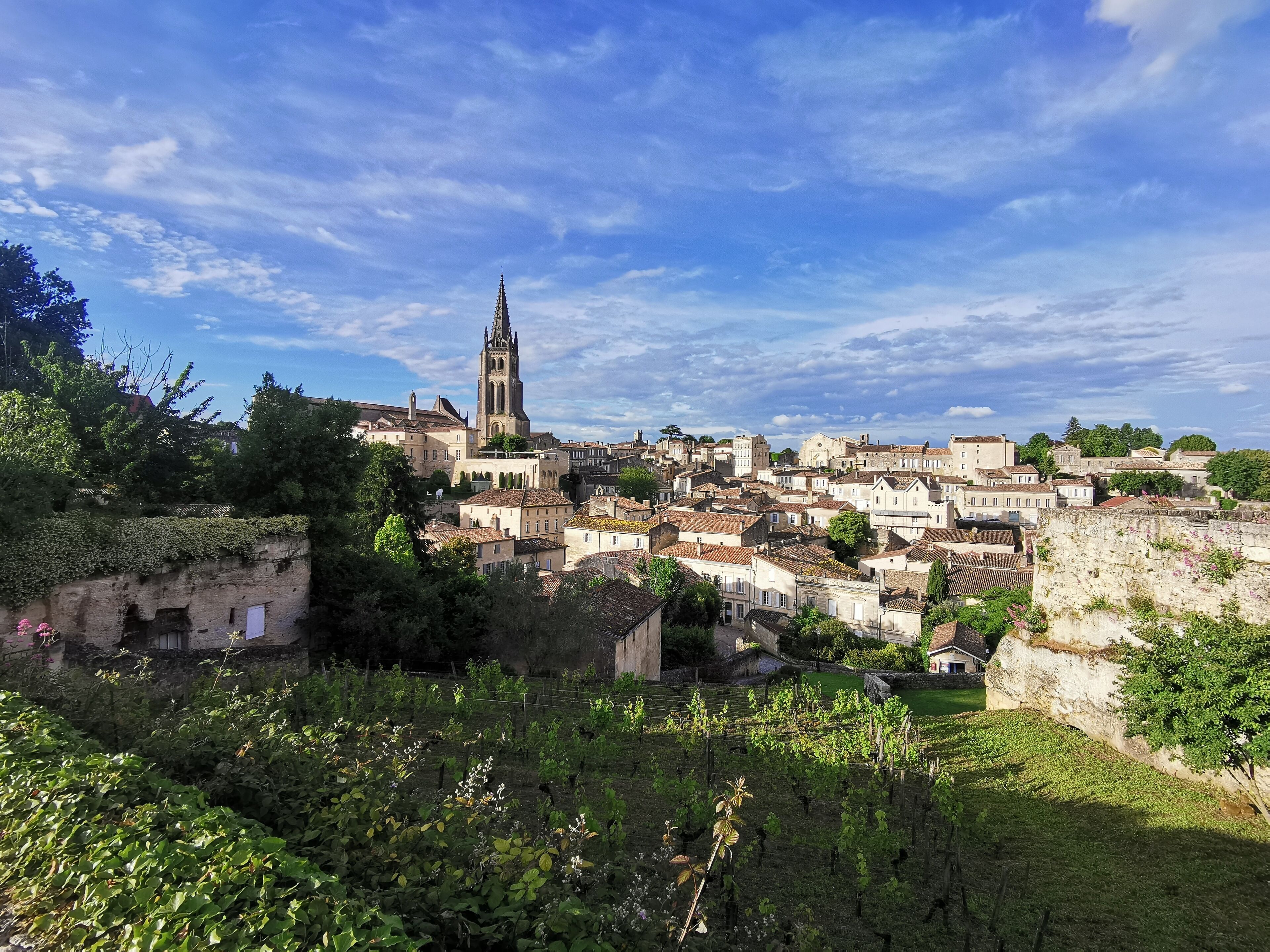 Uma cidade histórica com uma torre de igreja imponente, rodeada por edifícios tradicionais e vegetação exuberante.