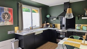 A compact kitchen with a window, a sink, a stove, and a dining area with chairs and a table. - Maison Finchette • 5 min f Saint-Émilion • Private Terrace • Parking • For 2 (Sainte-Terre)