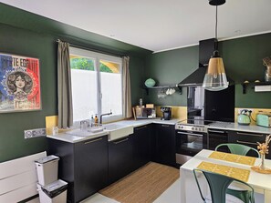 Cocina pequeña con ventana, un lavamanos, estufa y comedor con sillas y mesa.