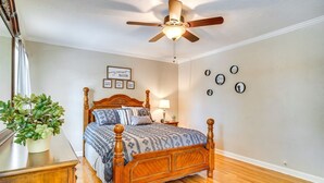 A bedroom with a wooden bed, a ceiling fan, a bedside table with a lamp, and a potted plant.
