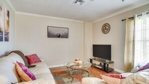 A living room with a beige sofa, a glass coffee table, a flat-screen TV, and a decorative clock on the wall.