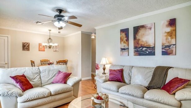 A living room with two sofas, a glass coffee table, a ceiling fan, and wall art.