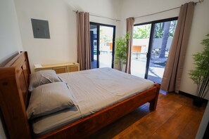 A bedroom with a wooden bed, a nightstand, and a potted plant. - Gey Tropical House (Liberia)