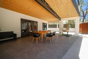 A modern outdoor dining area with a wooden table and chairs, a black sofa, and a hanging chair. - Gey Tropical House (Liberia)